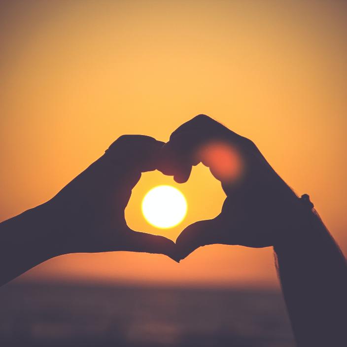 Zwei Hände formen ein Herz um die untergehende Sonne