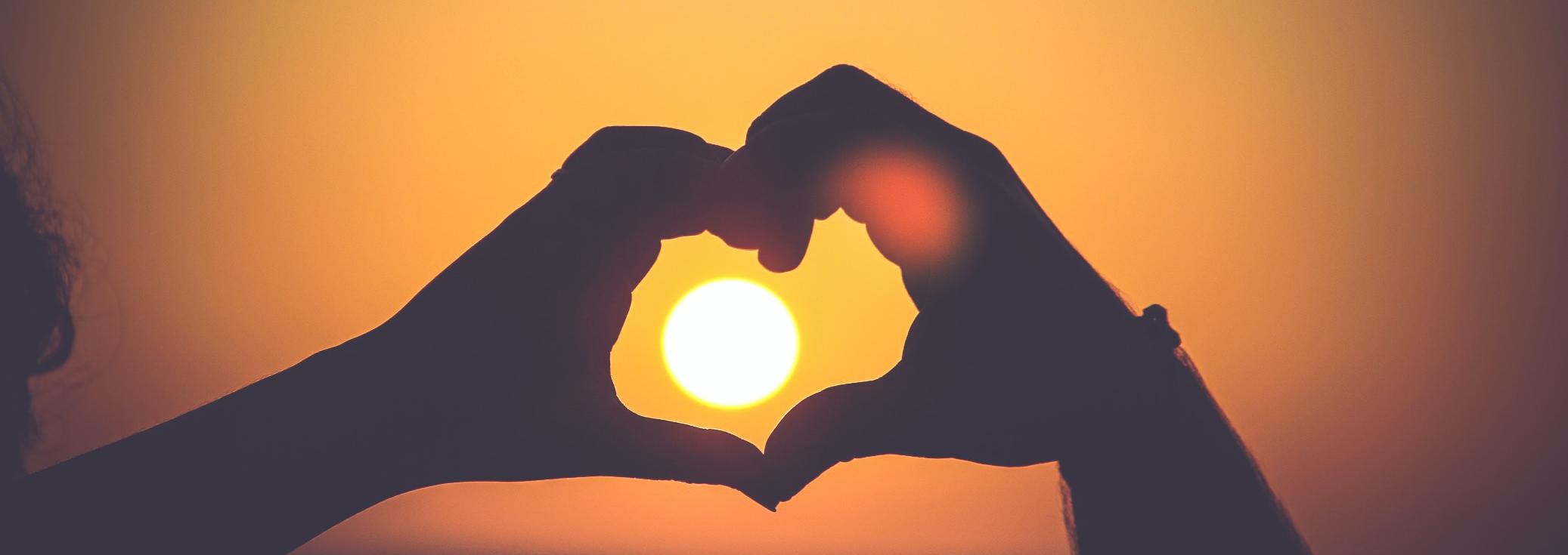 Zwei Hände formen ein Herz um die untergehende Sonne