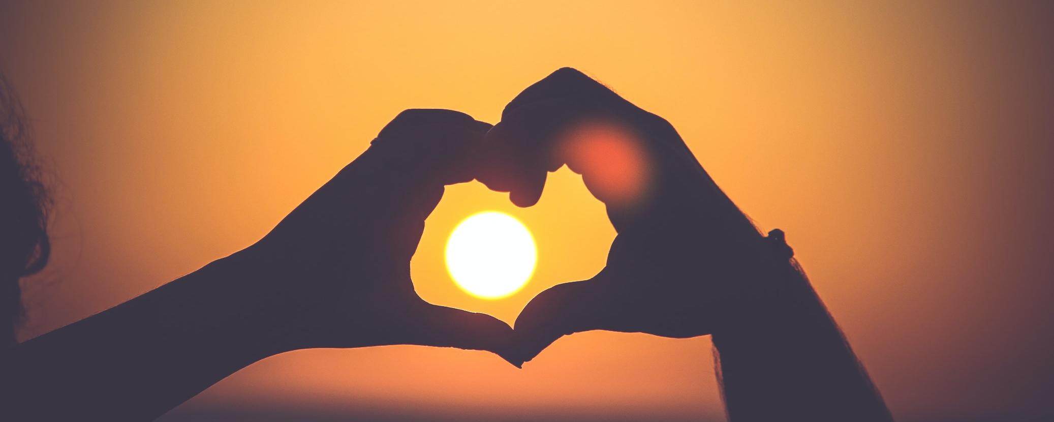 Zwei Hände formen ein Herz um die untergehende Sonne