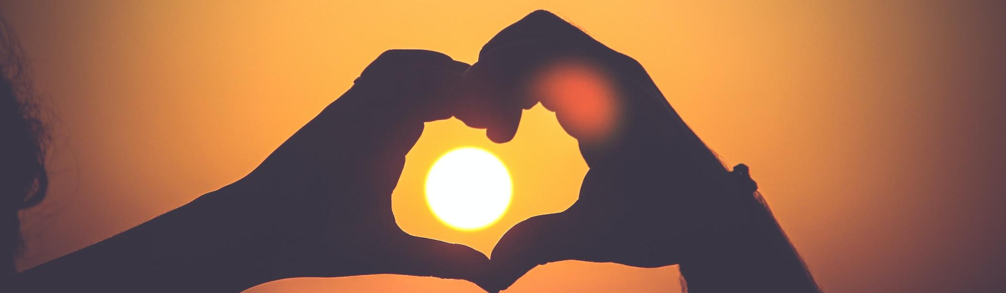 Zwei Hände formen ein Herz um die untergehende Sonne