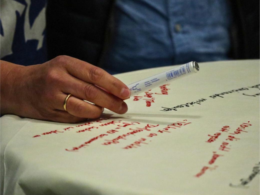Ein Flipchartblatt liegt auf einem Tisch, es ist beschrieben. Eine Hand mit Stift schwebt darüber.