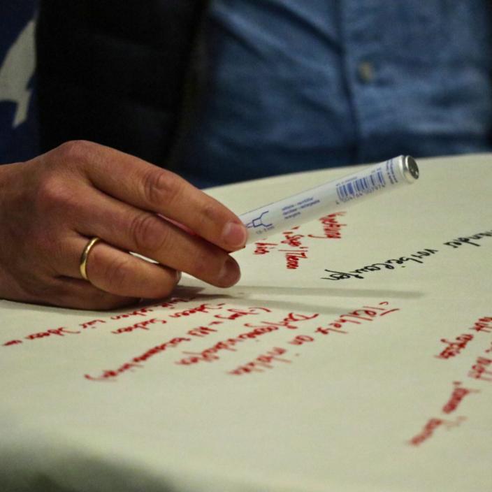 Ein Flipchartblatt liegt auf einem Tisch, es ist beschrieben. Eine Hand mit Stift schwebt darüber.