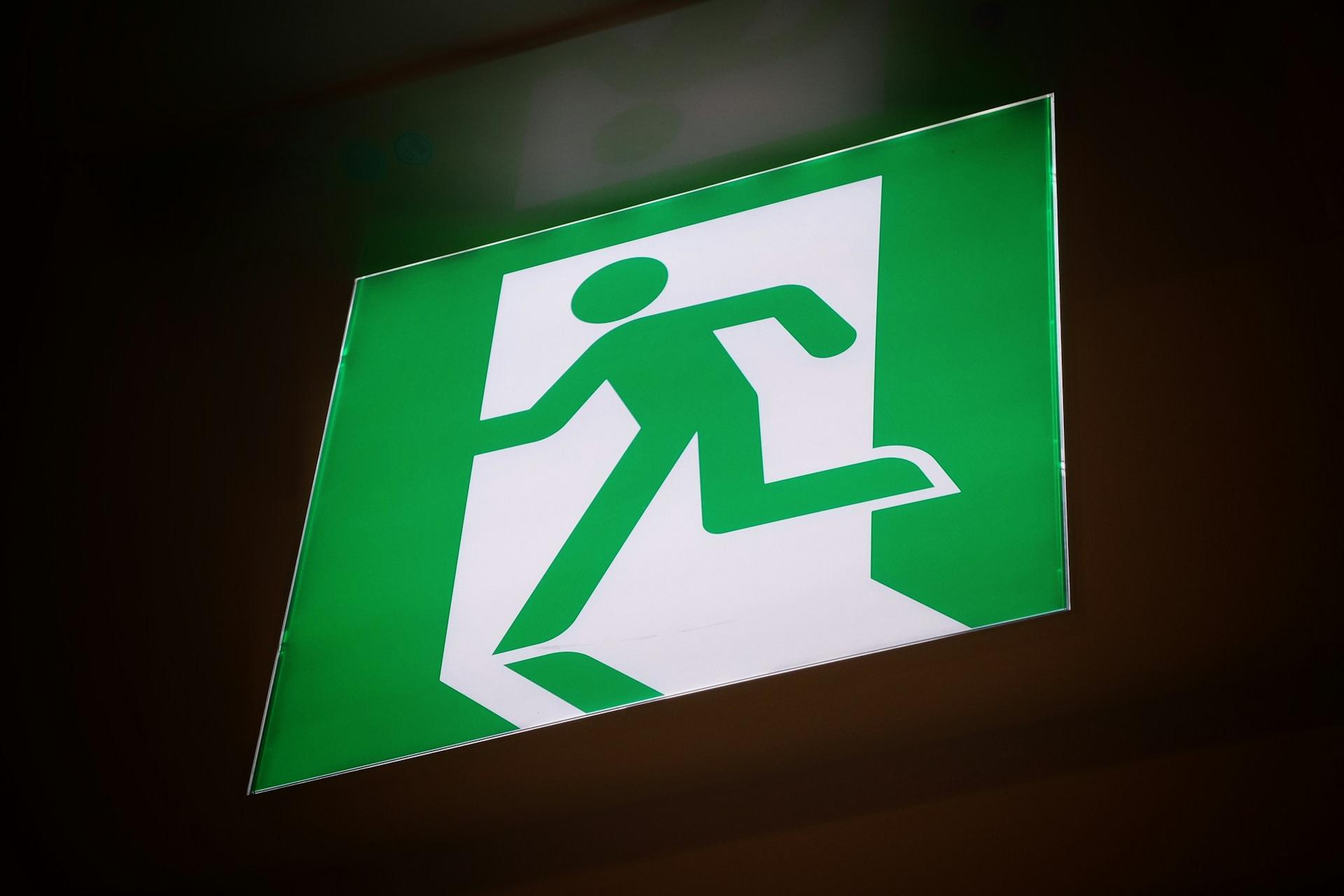 Exit-Schild, eine grüne Figur läuft durch eine weiße Tür. Hinweis auf den Notausgang