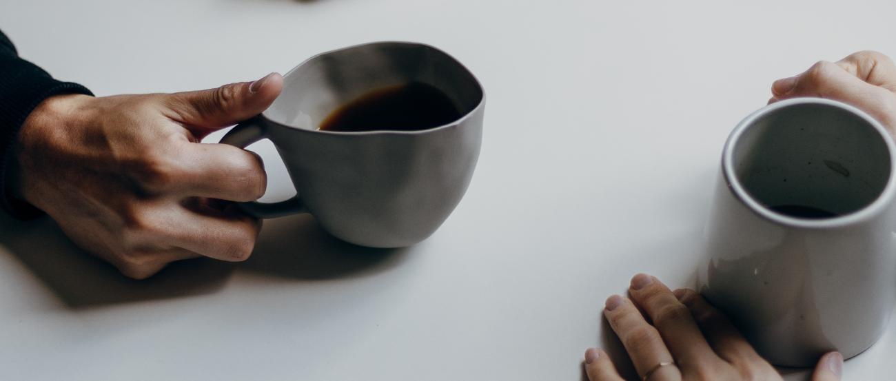Auf einem Tisch stehen zwei Tassen Kaffee, daneben sind die Hände der Personen zu sehen, die am Tisch sitzen.
