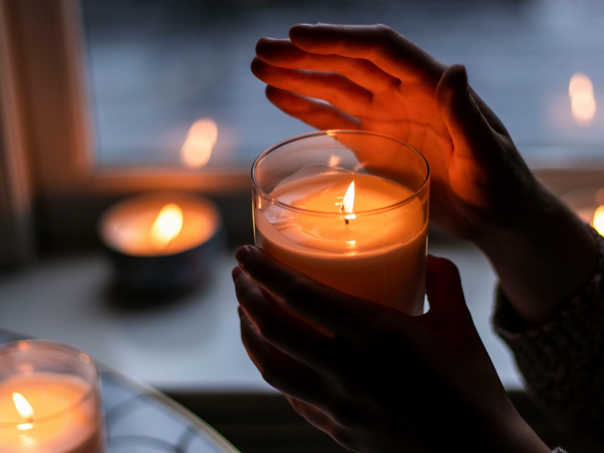 Eine Hand hält eine brennende Kerze in einem Glas und die andere Hand ist schützend über die Flamme gehalten