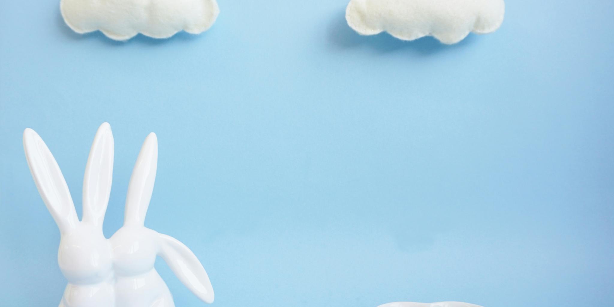 Auf einem hellblauen Untergrund stehen zwei Osterhasen und Spiegeleier als Süßigkeiten. Im Hintergrund sind zwei Wolken