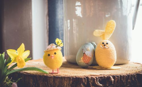 Auf einer Baumscheibe steht ein kleines gebasteltes Küken und ein Osterhase, der aus einem Ei gebastelt wurde