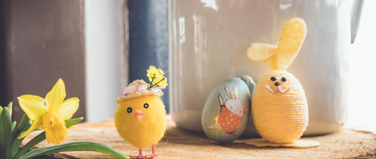 Auf einer Baumscheibe steht ein kleines gebasteltes Küken und ein Osterhase, der aus einem Ei gebastelt wurde