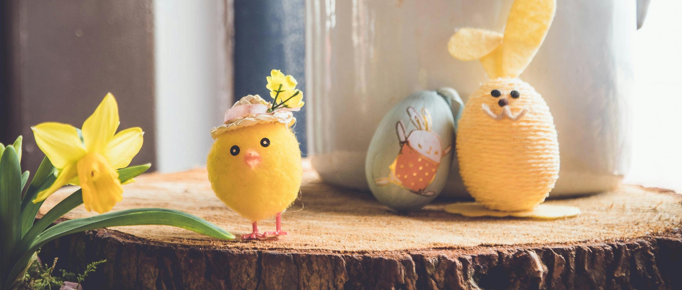Auf einer Baumscheibe steht ein kleines gebasteltes Küken und ein Osterhase, der aus einem Ei gebastelt wurde