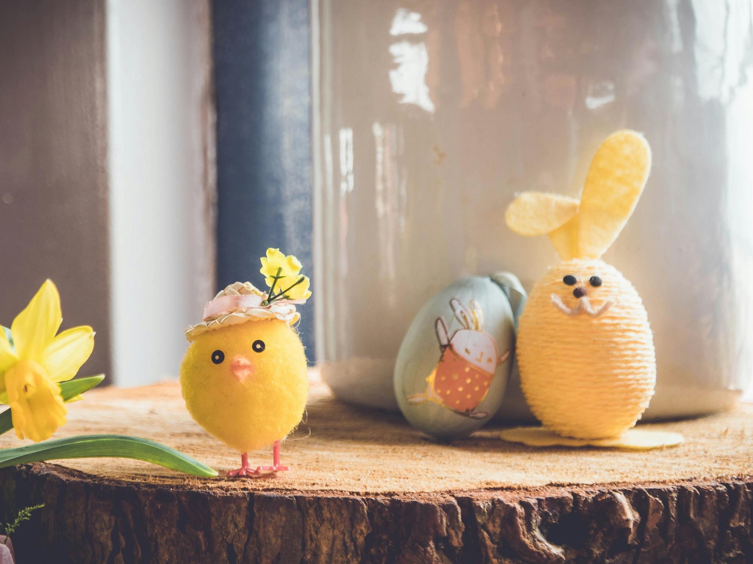 Auf einer Baumscheibe steht ein kleines gebasteltes Küken und ein Osterhase, der aus einem Ei gebastelt wurde