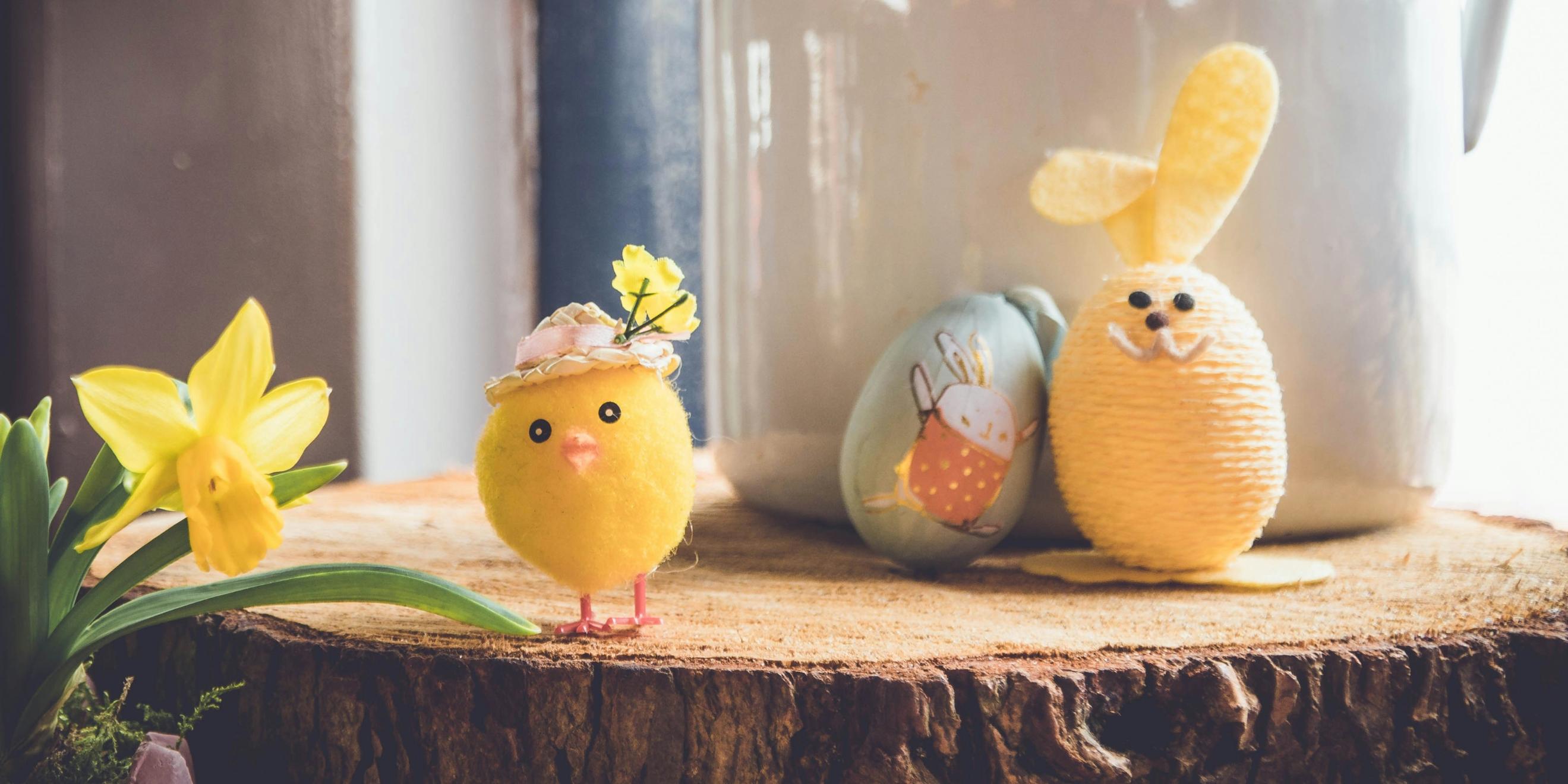Auf einer Baumscheibe steht ein kleines gebasteltes Küken und ein Osterhase, der aus einem Ei gebastelt wurde