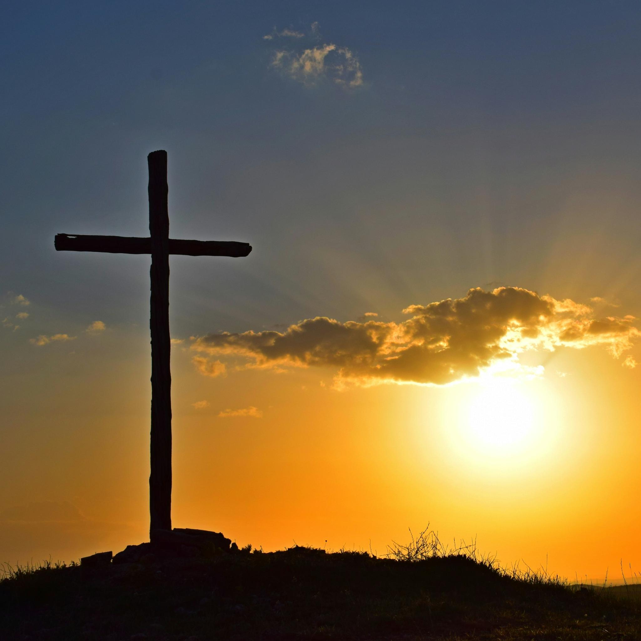 Blick in einen Sonnenuntergang. Auf einem kleinen Hügel steht in Kreuz, es ist nur als Silhouette zu sehen