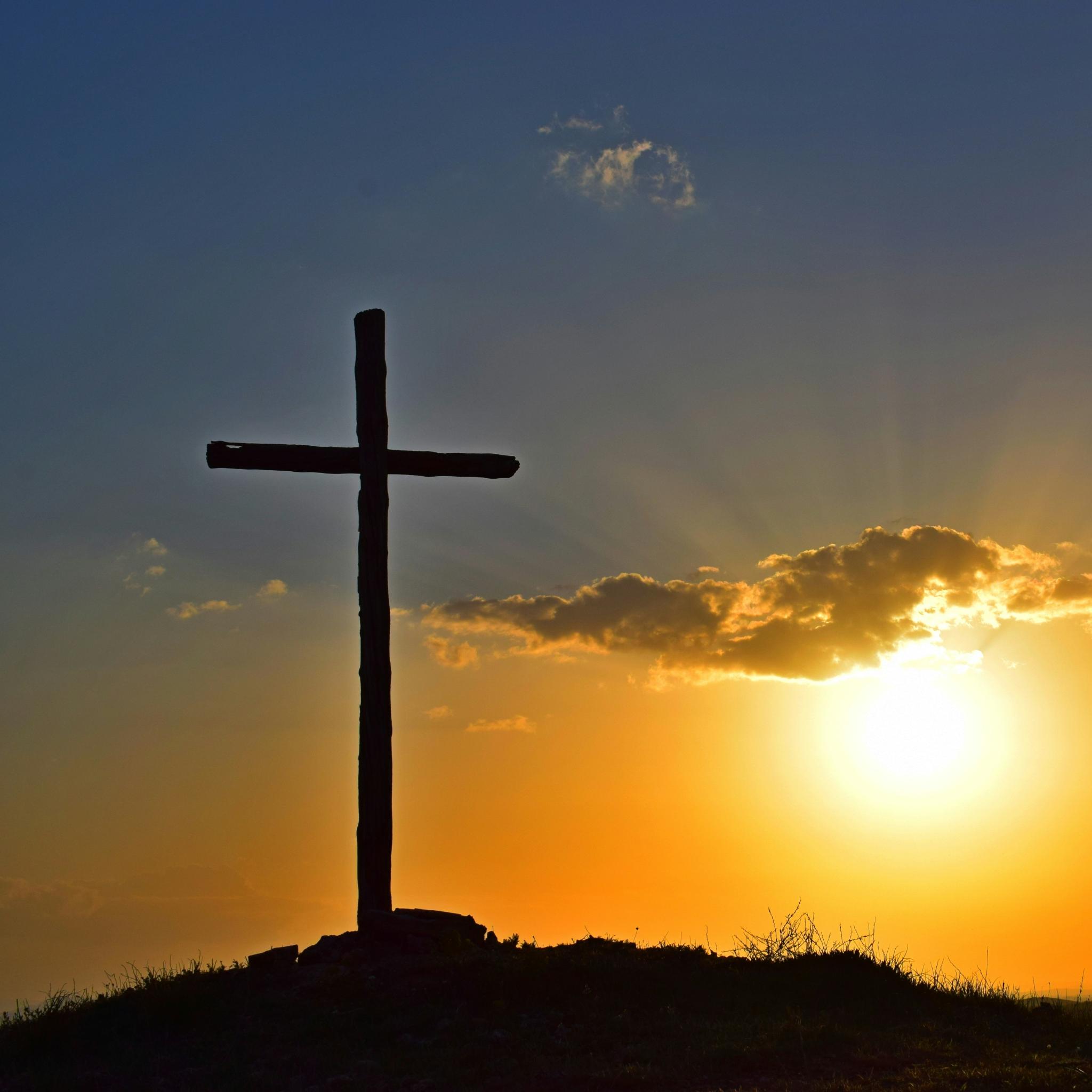 Blick in einen Sonnenuntergang. Auf einem kleinen Hügel steht in Kreuz, es ist nur als Silhouette zu sehen