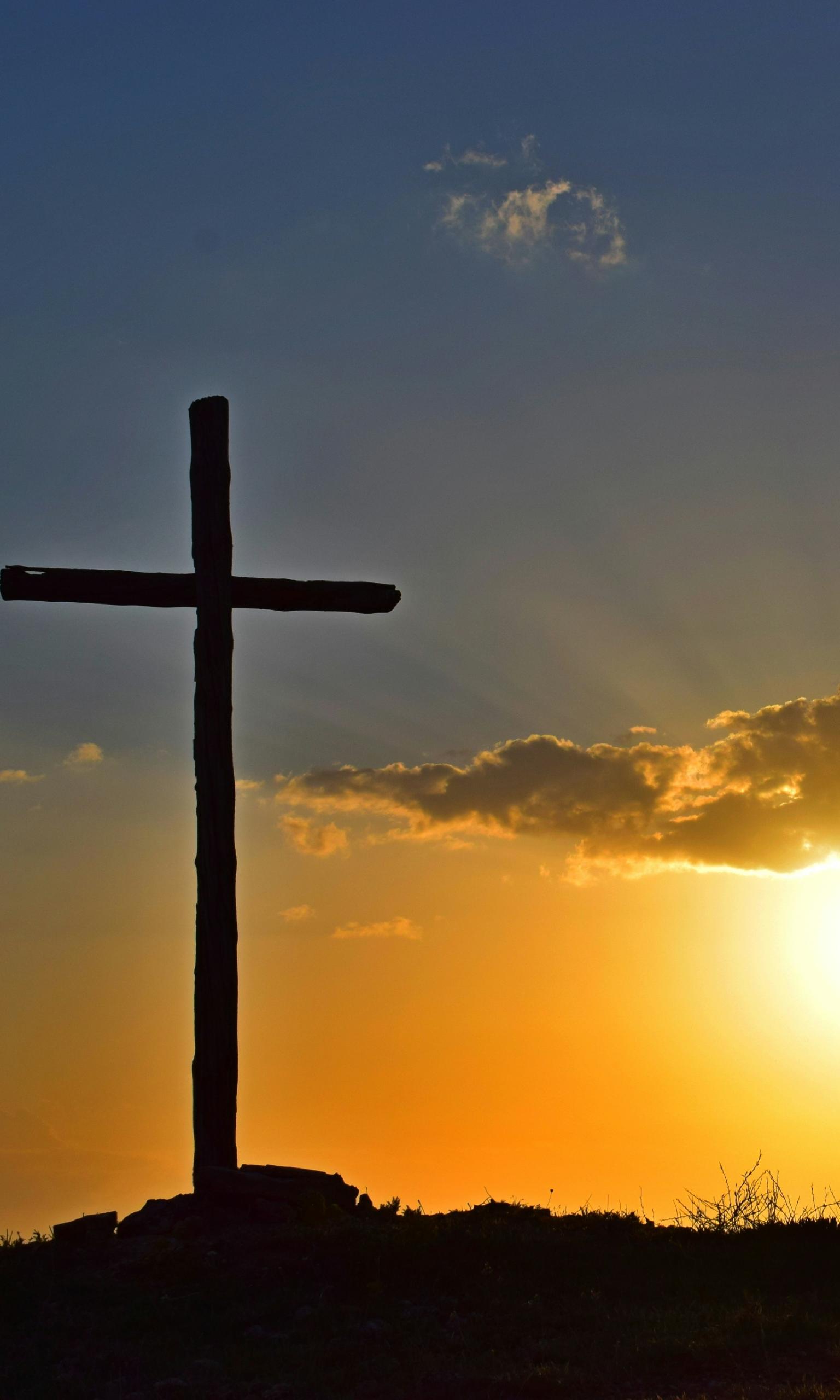 Blick in einen Sonnenuntergang. Auf einem kleinen Hügel steht in Kreuz, es ist nur als Silhouette zu sehen