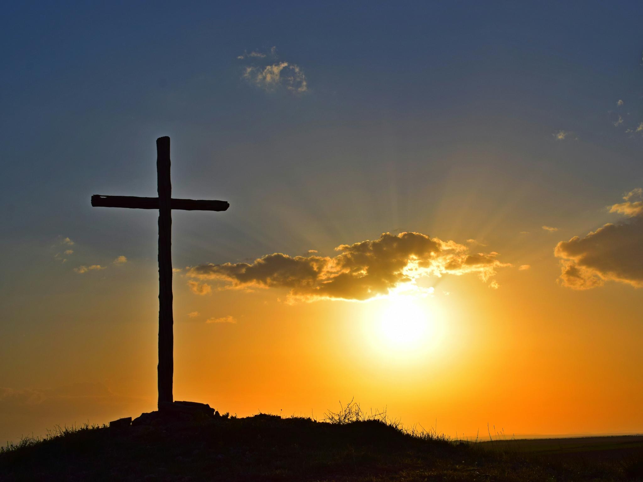 Blick in einen Sonnenuntergang. Auf einem kleinen Hügel steht in Kreuz, es ist nur als Silhouette zu sehen