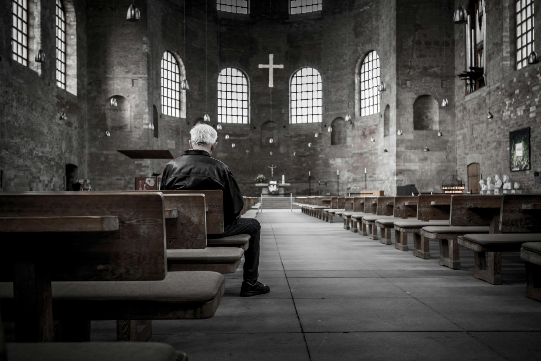 Ein Mann sitzt in einer Kircher auf einer Kirchenbank. Der Mann ist nur von hinten zu sehen. Das Bild ist schwarz weiß