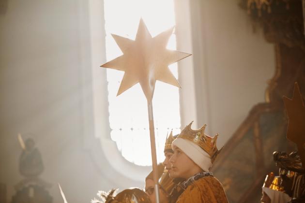 Blick auf ein weißes Kirchenfenster. Davor stehen Sternsinger, die einen Stern vor das Fenster halten