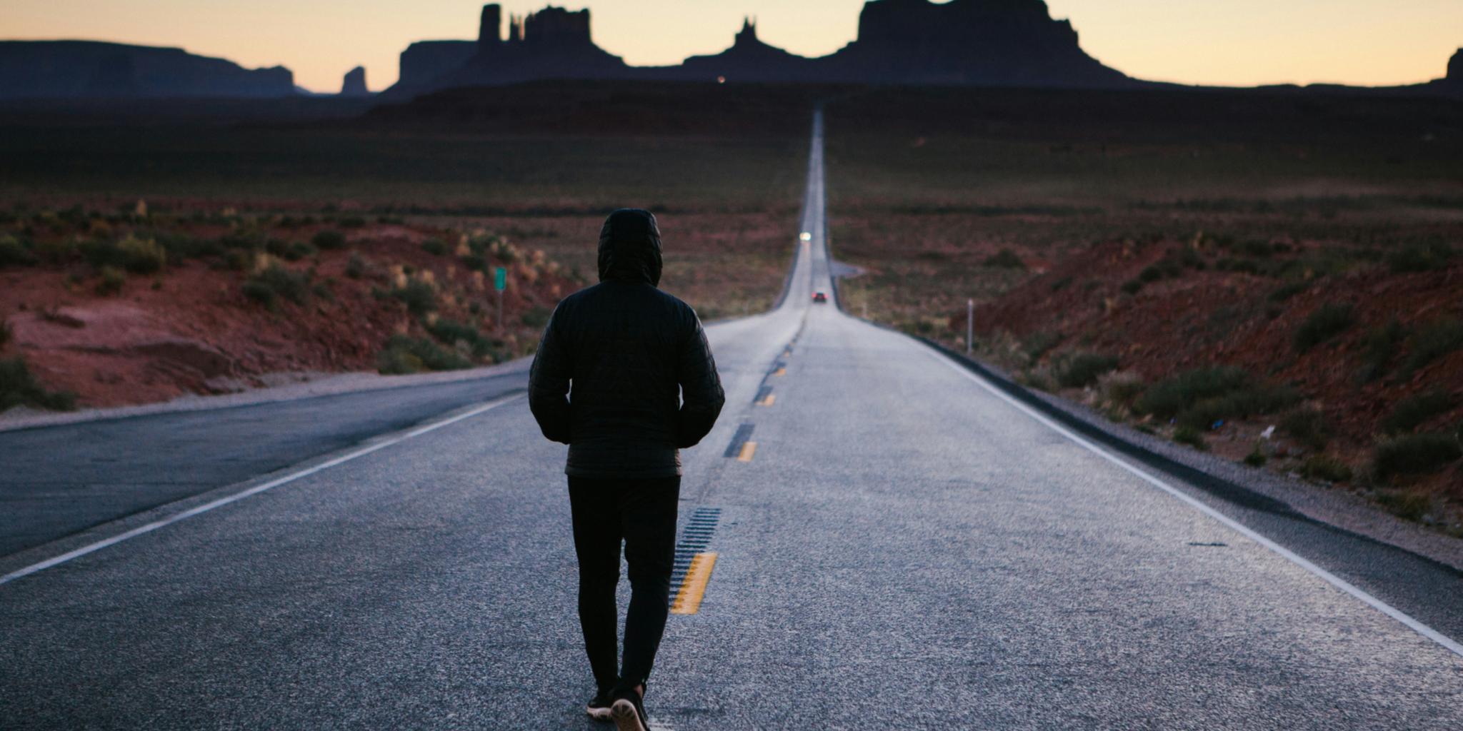 Ein Mann geht auf einer verlassenen Straße, um ihn herum ist nur Landschaft