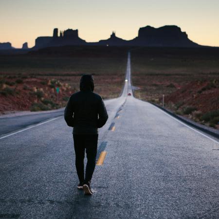 Ein Mann geht auf einer verlassenen Straße, um ihn herum ist nur Landschaft