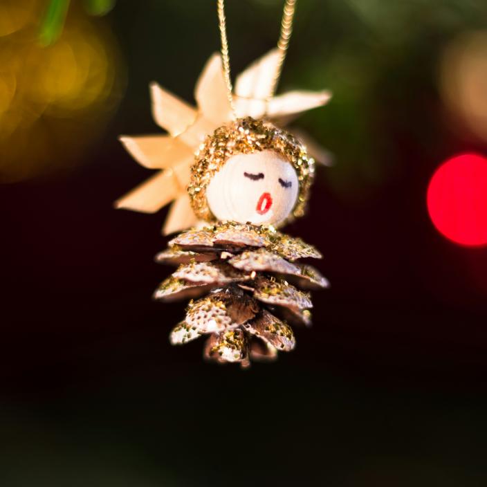 Ein Tannenzapfen, aus dem ein Engel gebastelt wurde, hängt an einem Weihnachtsbaum
