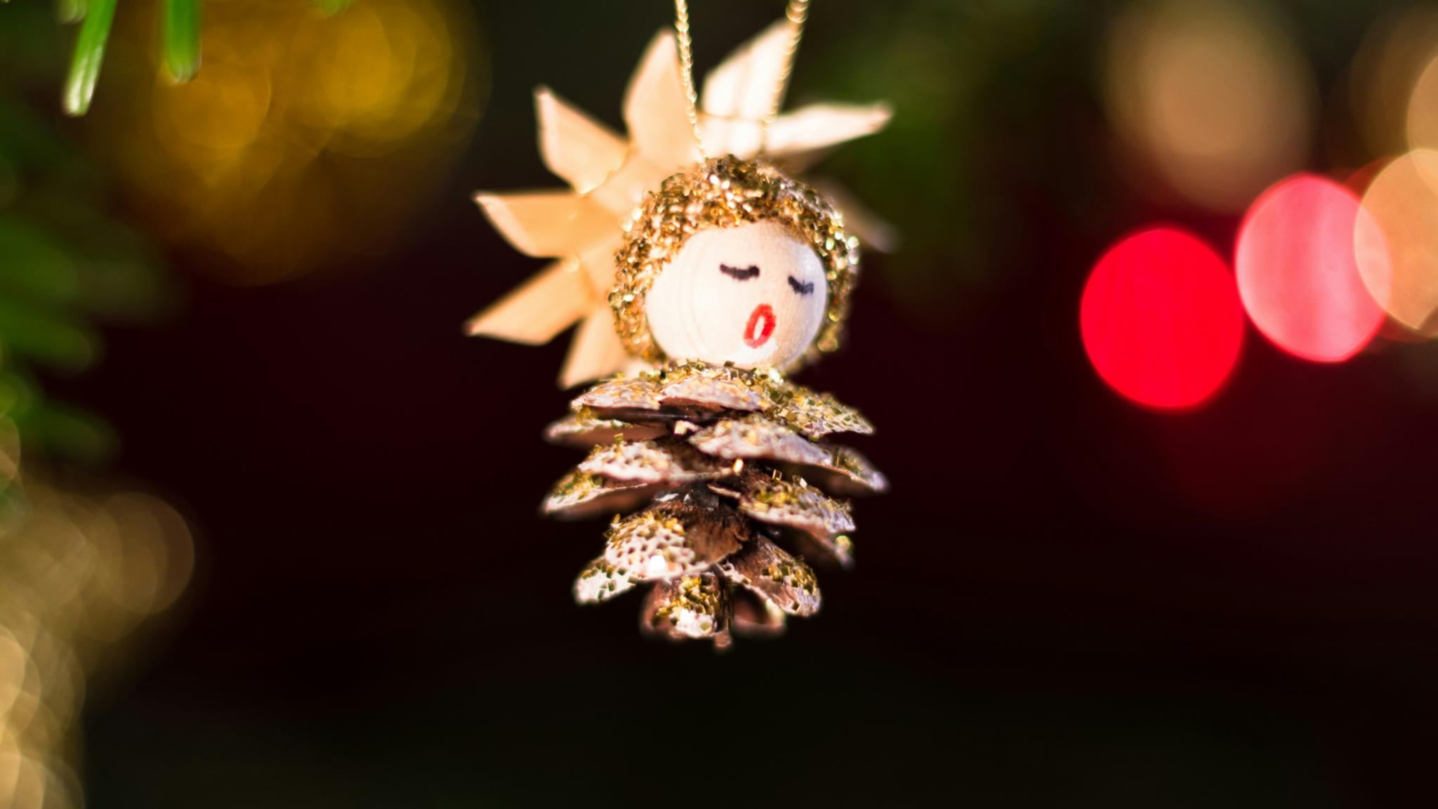 Ein Tannenzapfen, aus dem ein Engel gebastelt wurde, hängt an einem Weihnachtsbaum