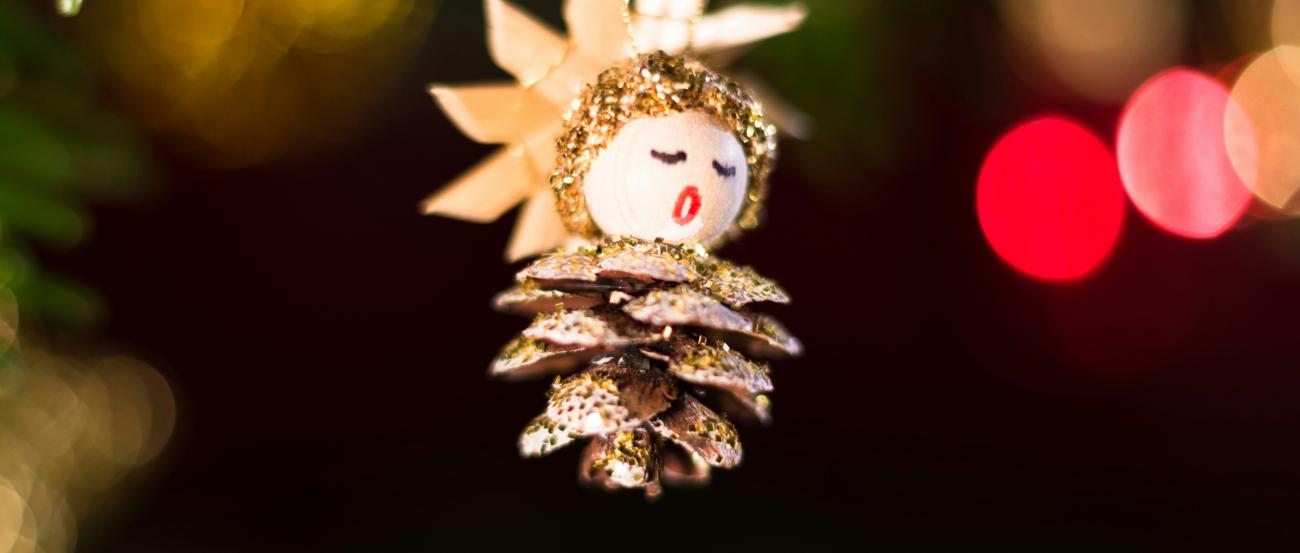 Ein Tannenzapfen, aus dem ein Engel gebastelt wurde, hängt an einem Weihnachtsbaum