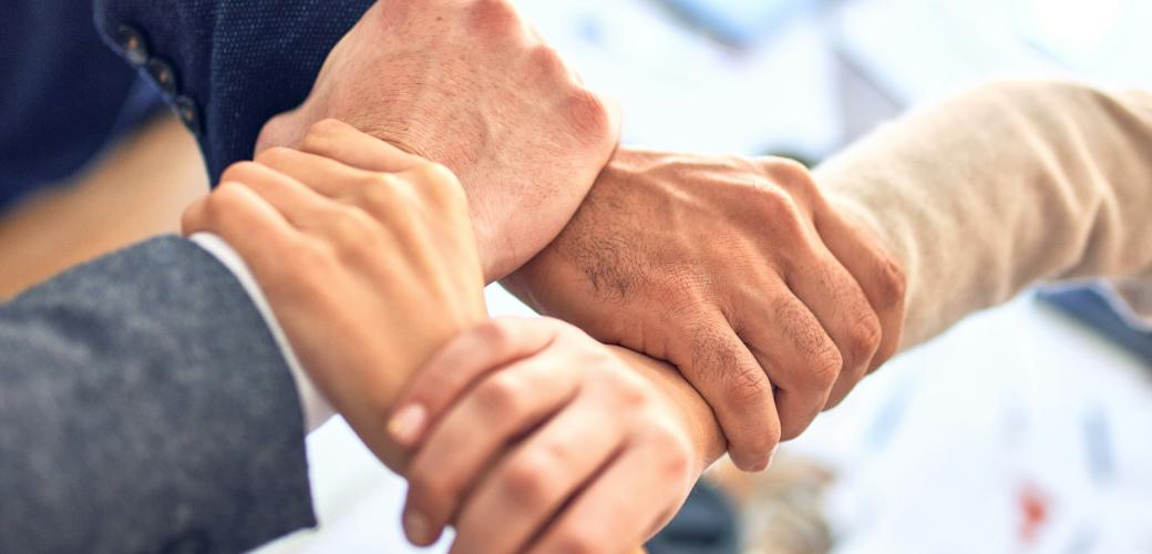 vier Hände greifen ein anderes Handgelenk, so dass eine stabile Fläche entsteht