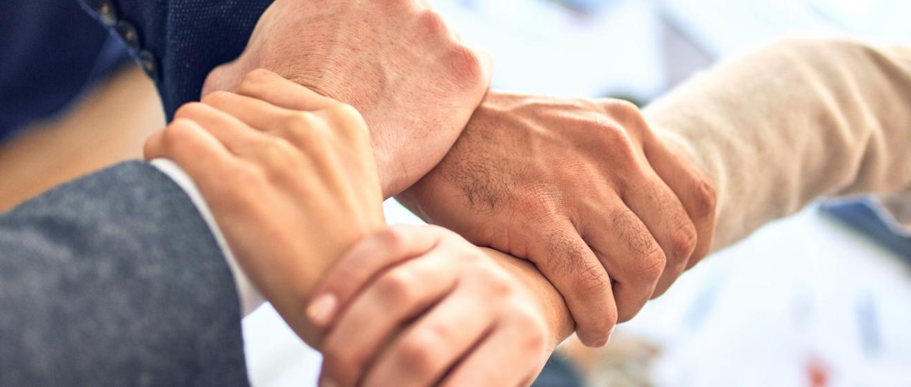 vier Hände greifen ein anderes Handgelenk, so dass eine stabile Fläche entsteht