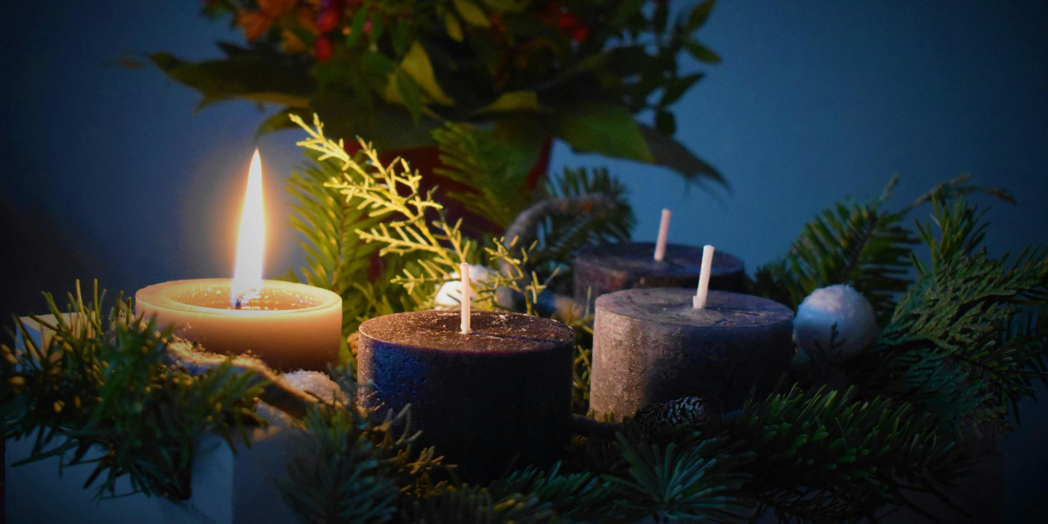 An einem Adventskranz brennt eine Kerze