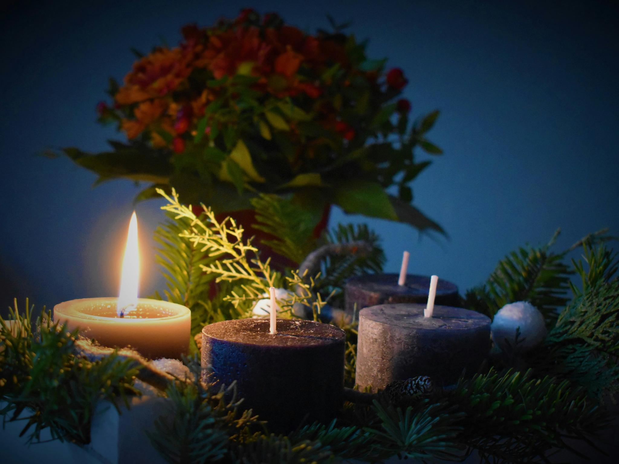 An einem Adventskranz brennt eine Kerze