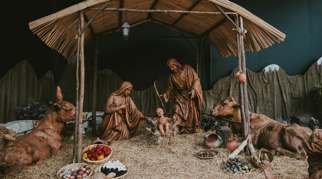 Eine Hütte aus Holz in der Josef und Maria um das Jesuskind stehen. Die Hütte ist beleuchtet, ebenso wie die Bäume im Hintergrund