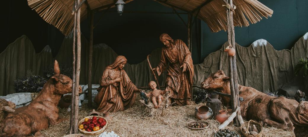 Eine Hütte aus Holz in der Josef und Maria um das Jesuskind stehen. Die Hütte ist beleuchtet, ebenso wie die Bäume im Hintergrund