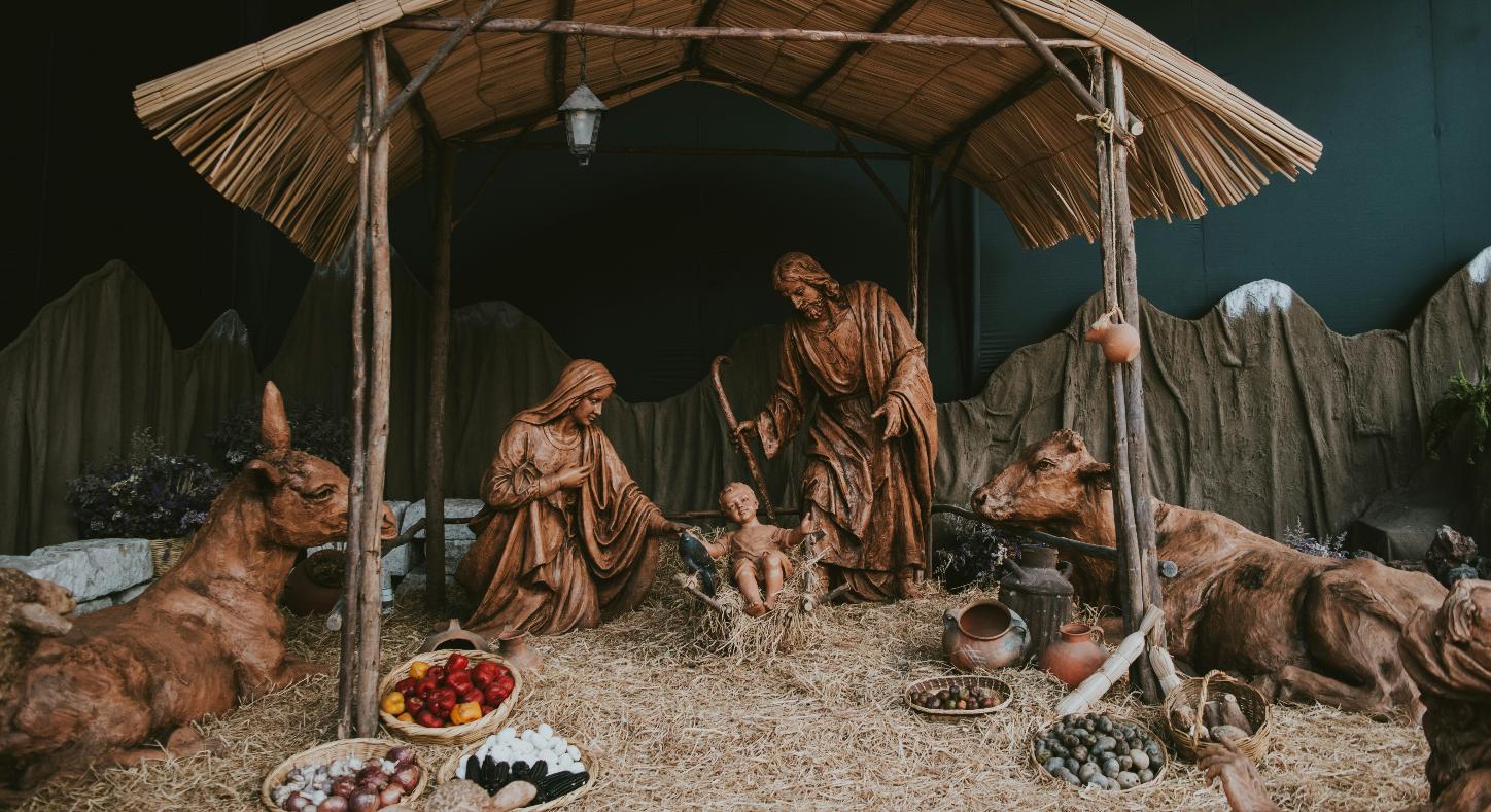 Eine Hütte aus Holz in der Josef und Maria um das Jesuskind stehen. Die Hütte ist beleuchtet, ebenso wie die Bäume im Hintergrund