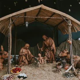 Eine Hütte aus Holz in der Josef und Maria um das Jesuskind stehen. Die Hütte ist beleuchtet, ebenso wie die Bäume im Hintergrund