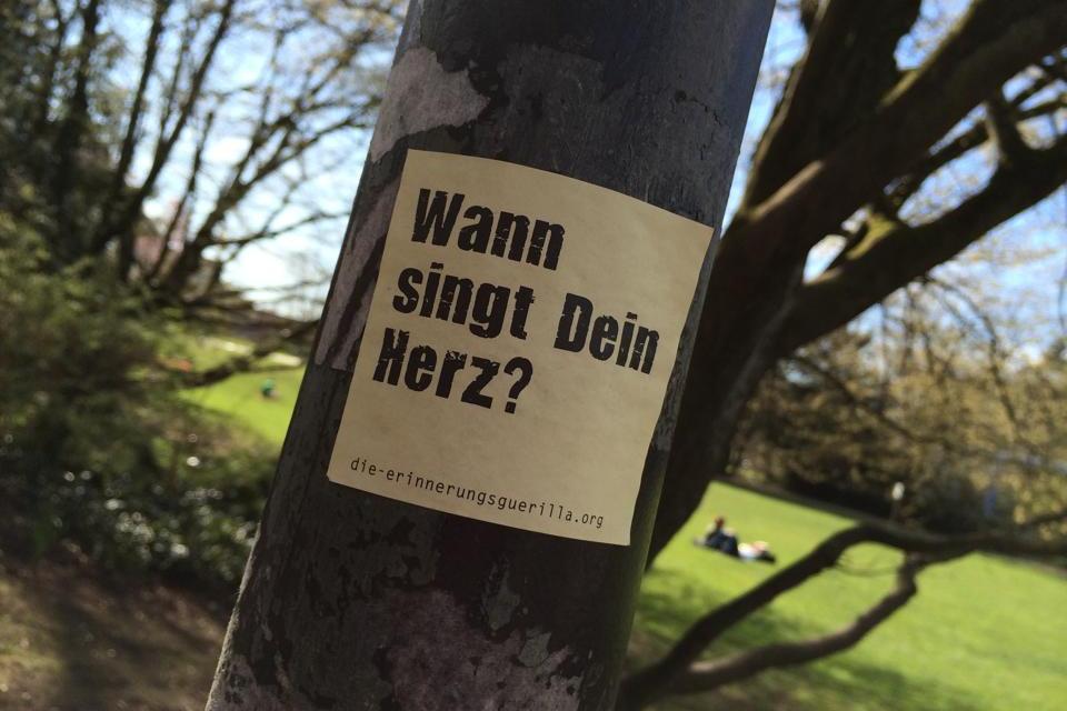Ein Aufkleber mit dem Text 'Wann singt Dein Herz?' klebt auf einem Laternenpfahl