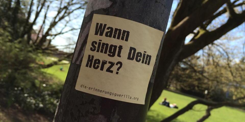 Ein Aufkleber mit dem Text 'Wann singt Dein Herz?' klebt auf einem Laternenpfahl