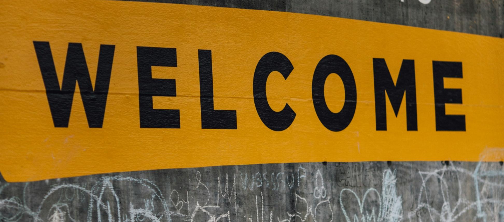 Auf einer Wand steht der Text 'Everyone is welcome'. Darunter sind viele kleine Kreidezeichnungen