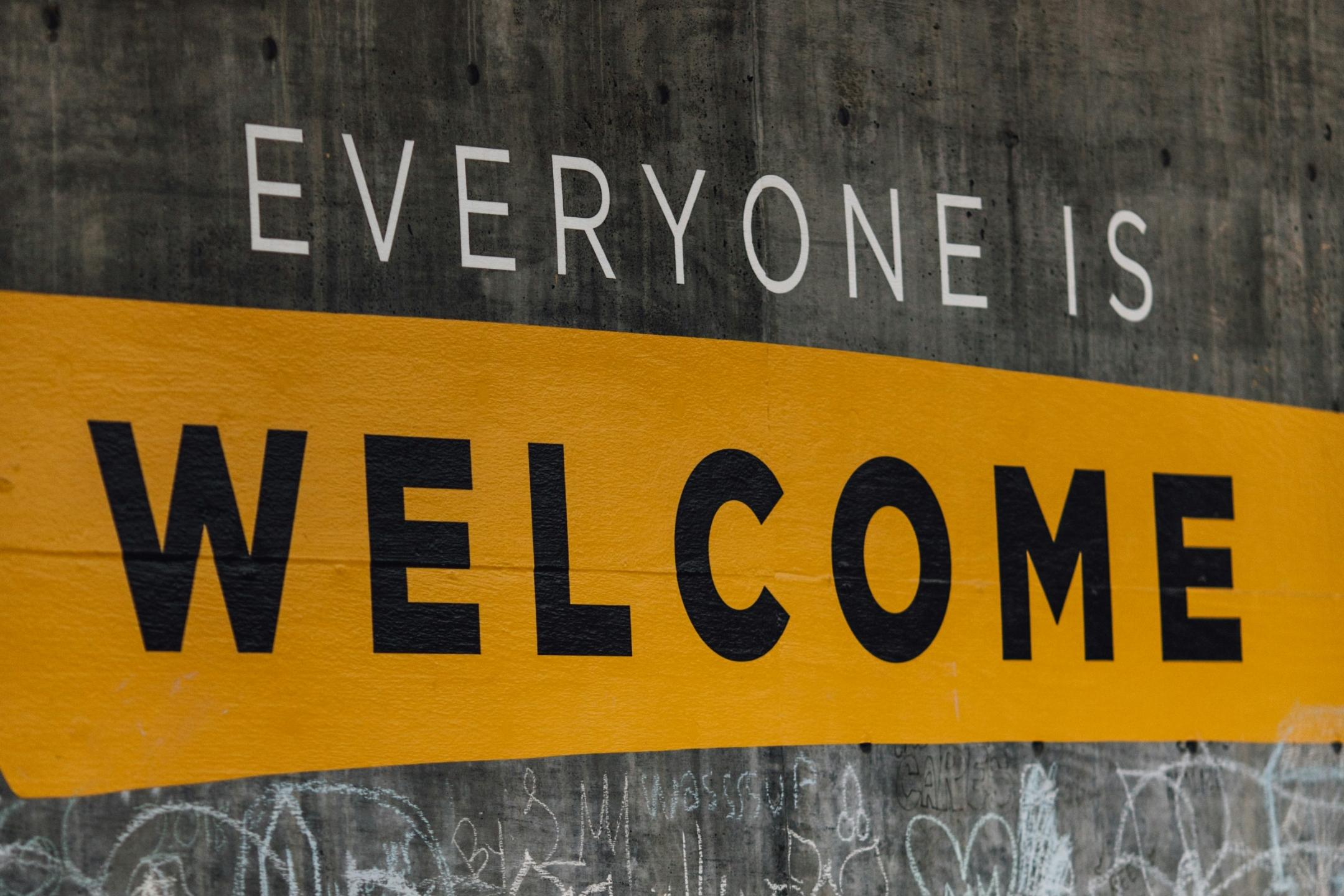 Auf einer Wand steht der Text 'Everyone is welcome'. Darunter sind viele kleine Kreidezeichnungen