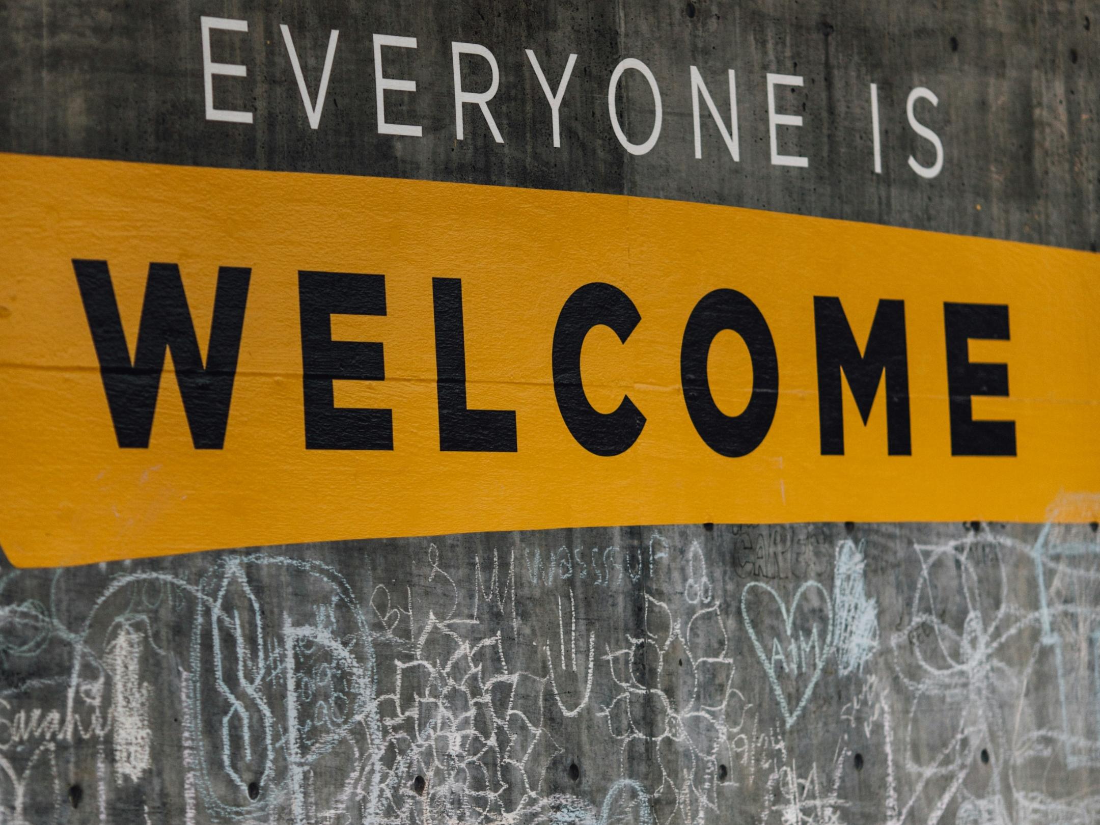 Auf einer Wand steht der Text 'Everyone is welcome'. Darunter sind viele kleine Kreidezeichnungen