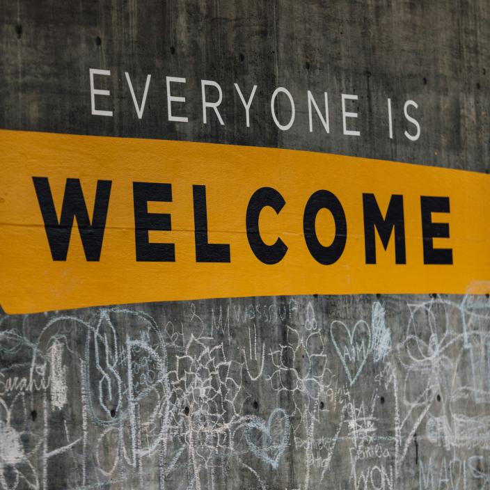 Auf einer Wand steht der Text 'Everyone is welcome'. Darunter sind viele kleine Kreidezeichnungen (c) Katie Moum auf Unsplash Auf einer Wand steht der Text 'Everyone is welcome'. Darunter sind viele kleine Kreidezeichnungen