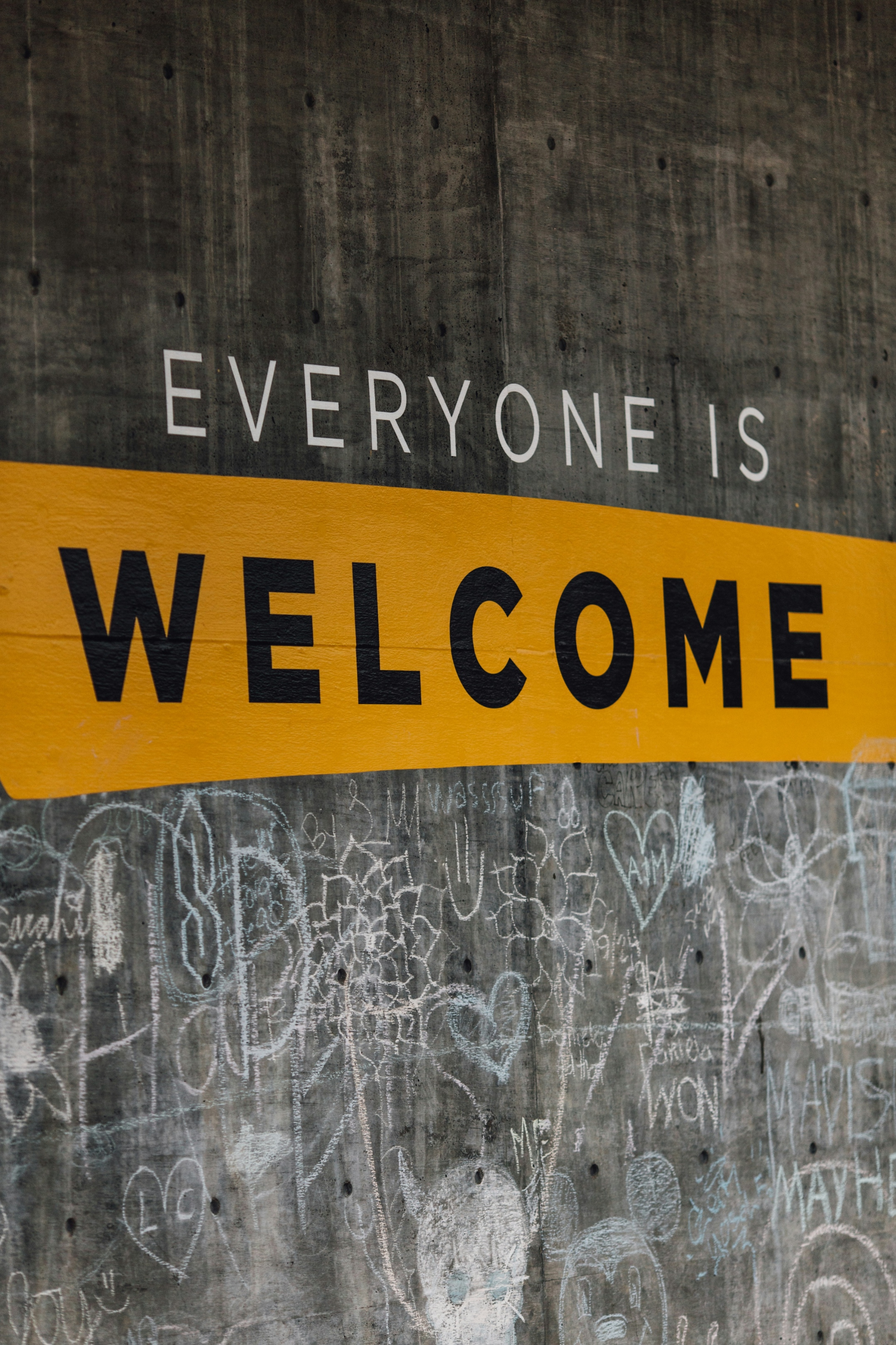 Auf einer Wand steht der Text 'Everyone is welcome'. Darunter sind viele kleine Kreidezeichnungen