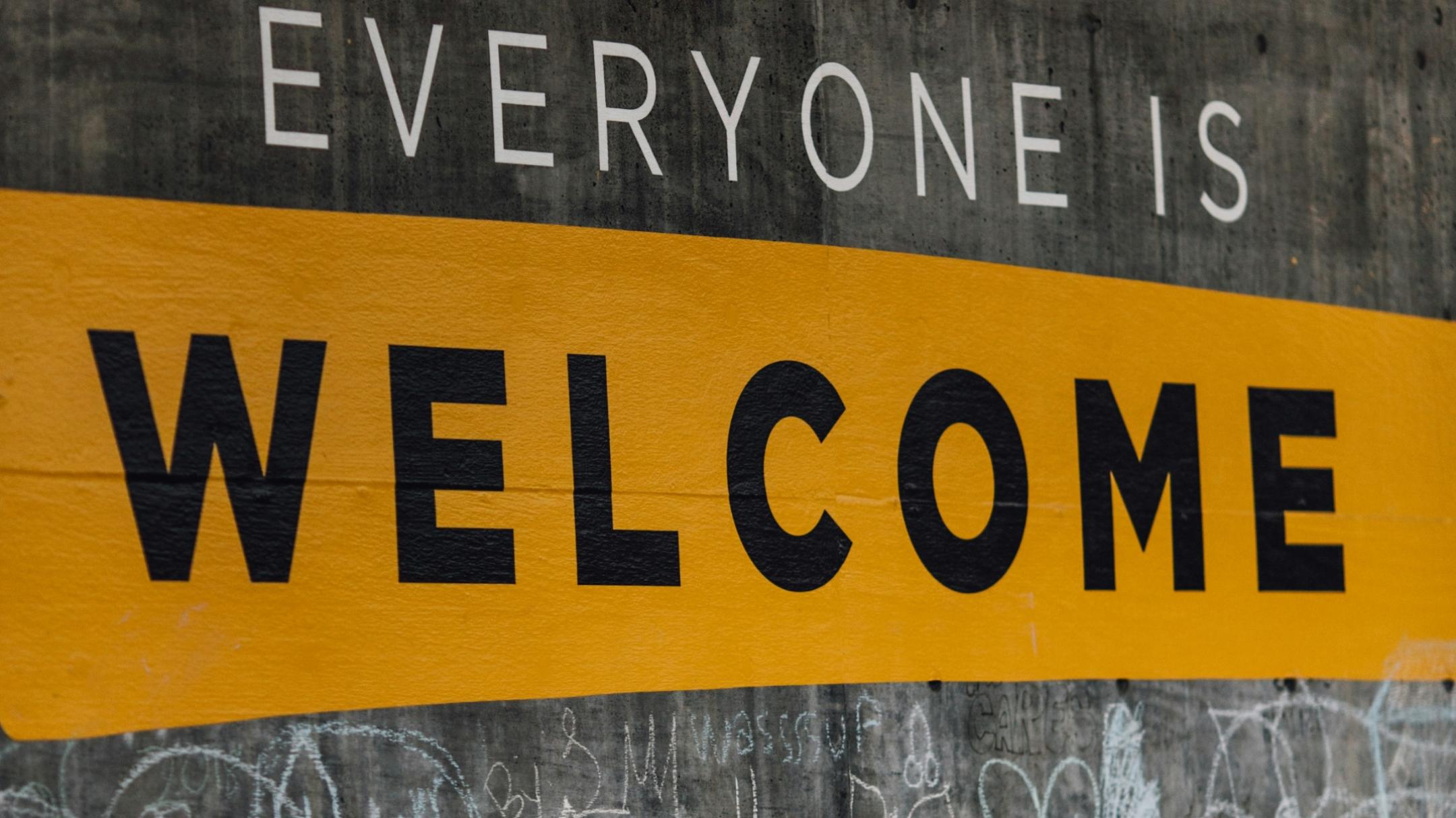 Auf einer Wand steht der Text 'Everyone is welcome'. Darunter sind viele kleine Kreidezeichnungen