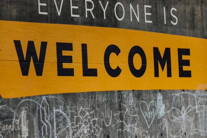 Auf einer Wand steht der Text 'Everyone is welcome'. Darunter sind viele kleine Kreidezeichnungen