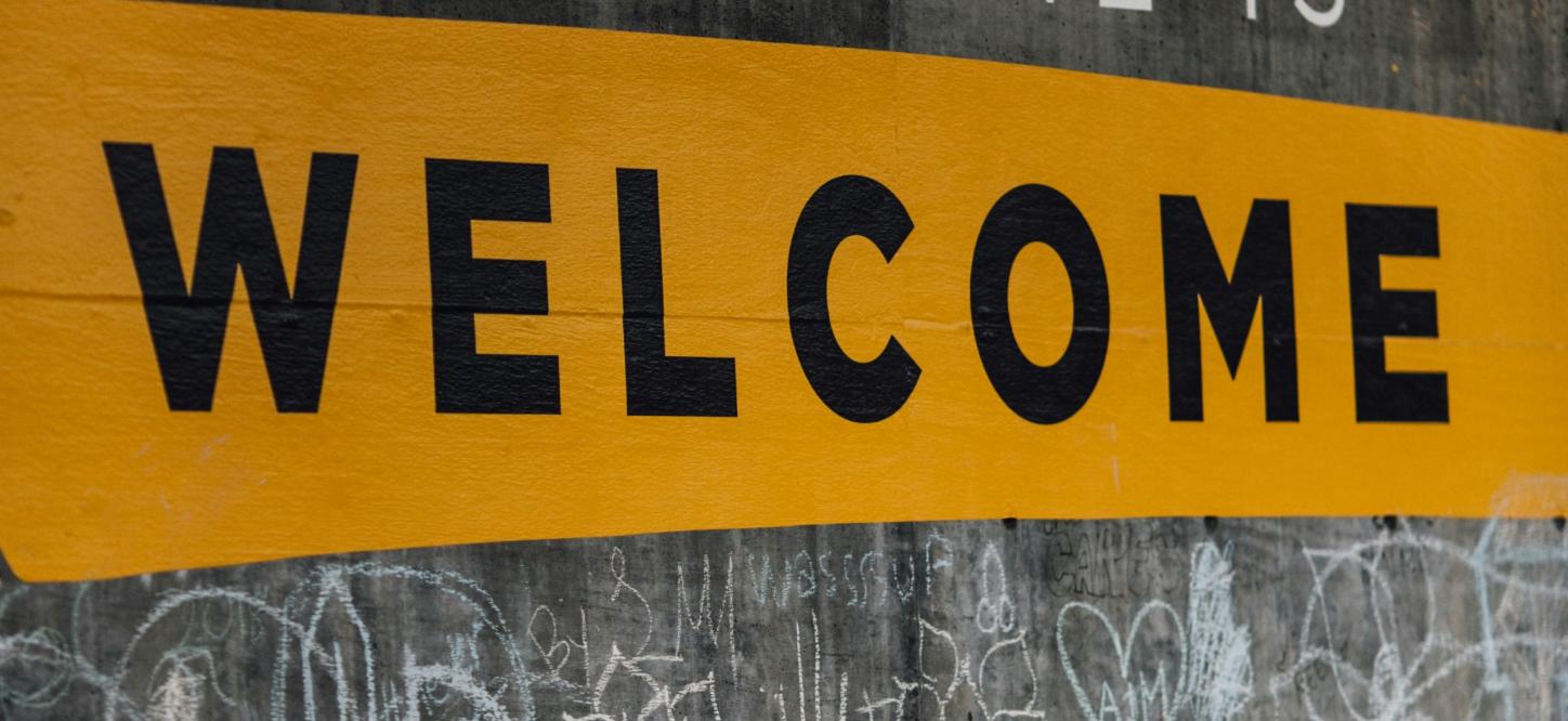 Auf einer Wand steht der Text 'Everyone is welcome'. Darunter sind viele kleine Kreidezeichnungen