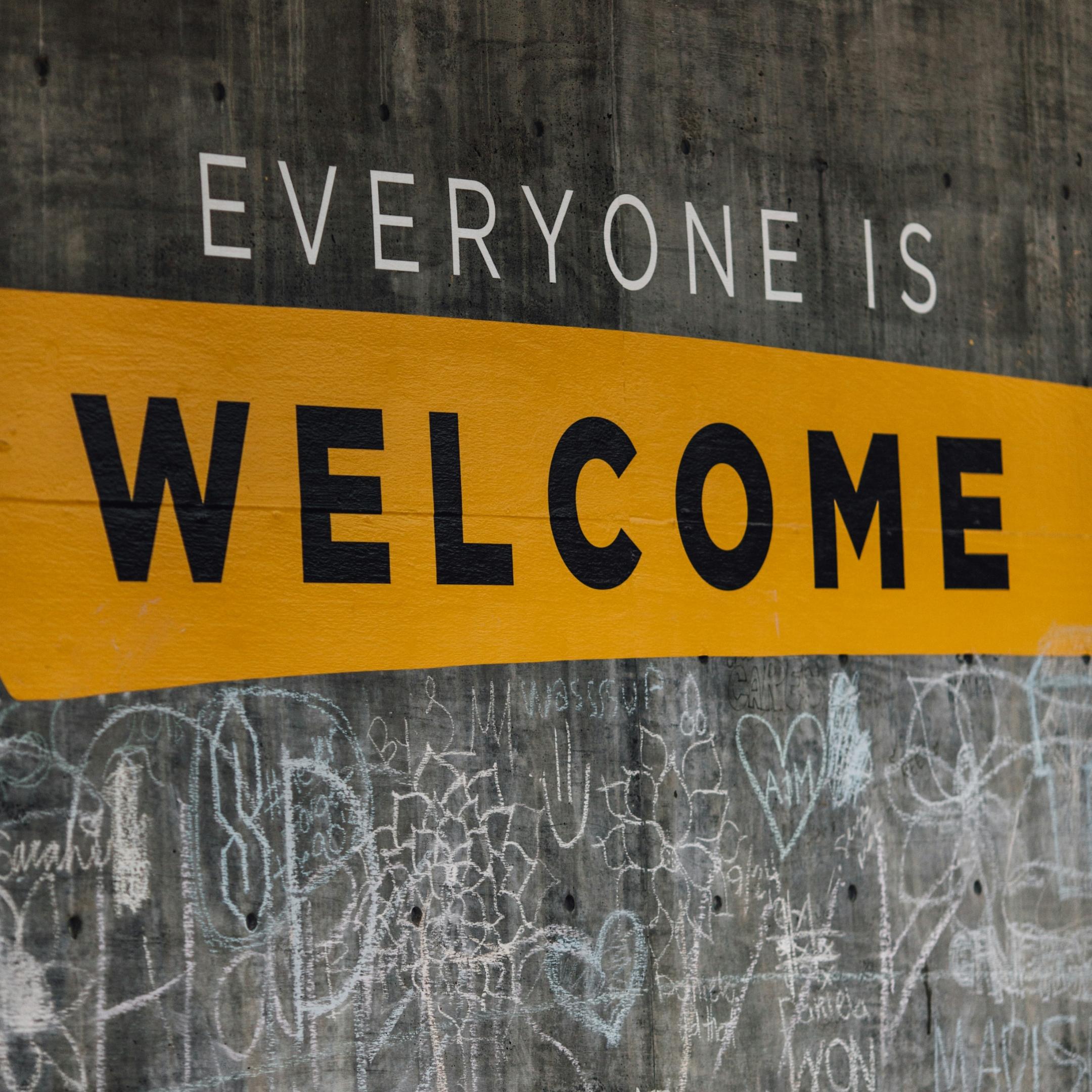 Auf einer Wand steht der Text 'Everyone is welcome'. Darunter sind viele kleine Kreidezeichnungen