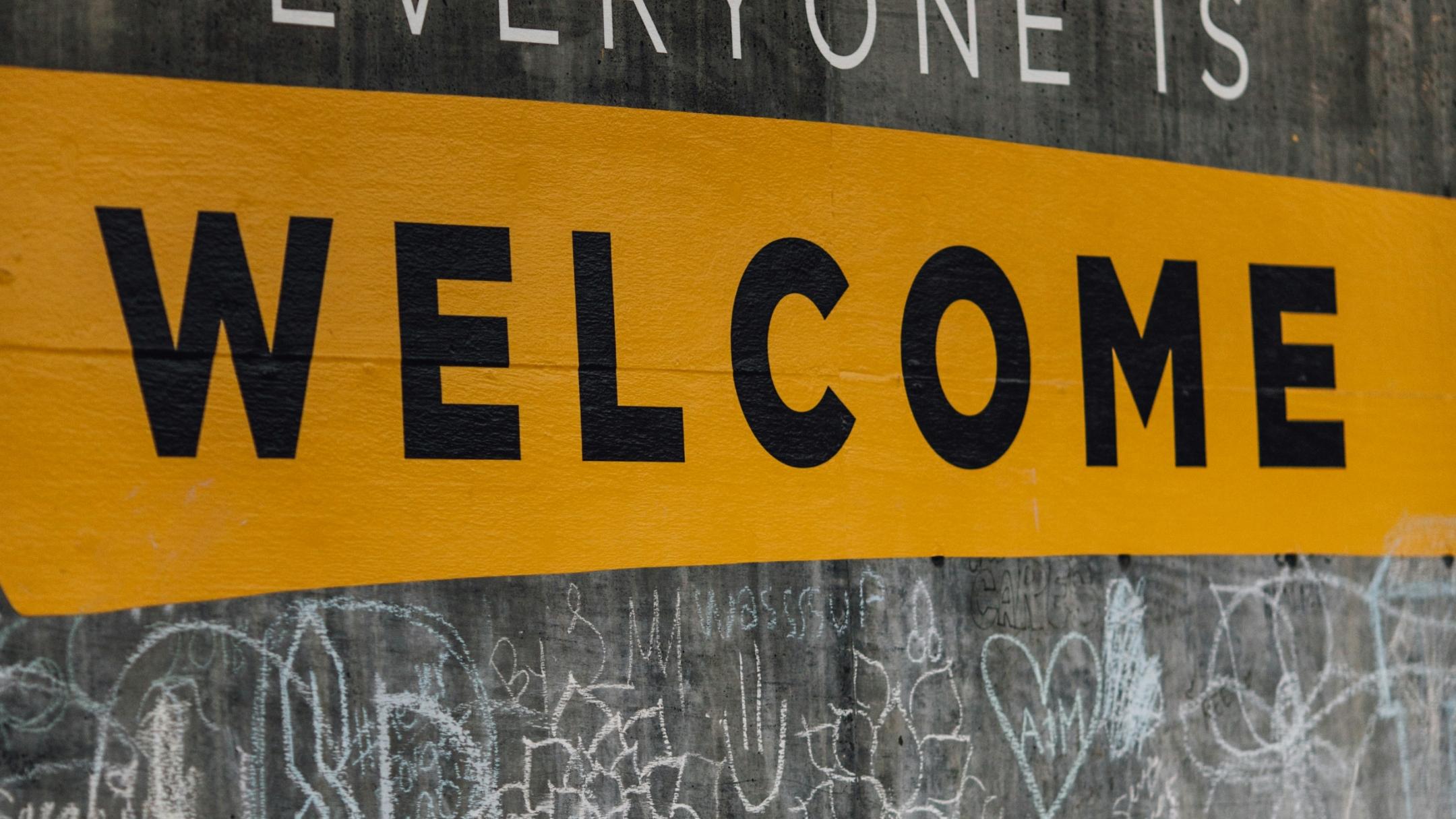 Auf einer Wand steht der Text 'Everyone is welcome'. Darunter sind viele kleine Kreidezeichnungen