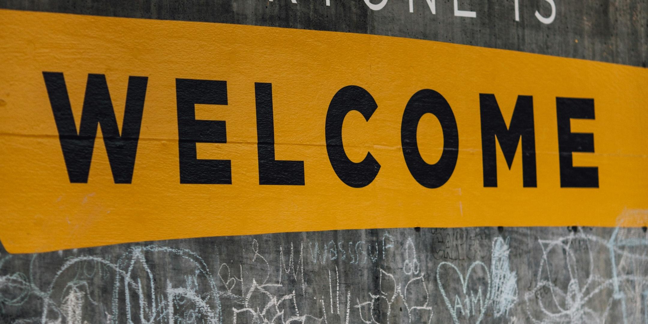 Auf einer Wand steht der Text 'Everyone is welcome'. Darunter sind viele kleine Kreidezeichnungen