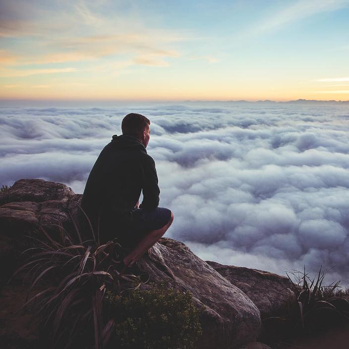 Mann sitzt auf einem Felsen über den Wolken