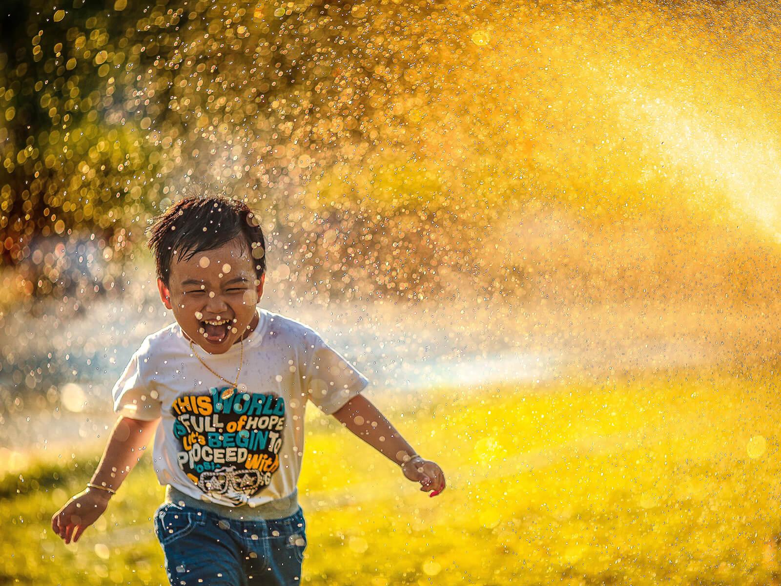 Kleiner Junge läuft durch das Wasser vom Rasensprenger
